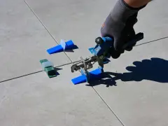 Mano con guanto usa pinza per livellare piastrelle, mostrando come tagliare piastrelle senza tagliapiastrelle con distanziatori.