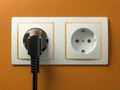 Dwa gniazdka elektryczne, jedno z wtyczką, na pomarańczowej ścianie. Typowe gniazdka w Hiszpanii.