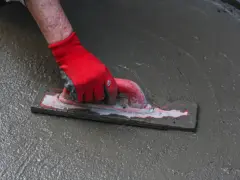 Ręka w czerwonej rękawicy wygładza świeżą wylewkę do garażu za pomocą kielni.