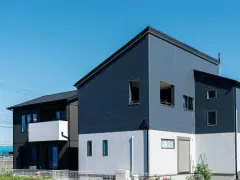 Nowoczesny dom z dwoma częściami, każda z innym dachem. Jedna część ma ciemny dach jednospadowy, druga zaś płaski.