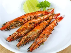Cuatro langostinos a la plancha, dorados y jugosos, servidos en plato blanco con rodaja de limón y perejil.