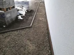 Stos **wapien** w budowie ścieżki wokół domu. Materiały budowlane leżą na ziemi, częściowo przykryte śniegiem.