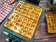 Frisch gebackene belgische Waffeln in einer Waffelform, daneben eine auf einem Rost.
