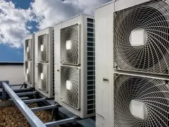 Rząd jednostek klimatyzacyjnych na dachu pod błękitnym niebem z chmurami.