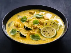 Aksamitne curry z kurczakiem, makaronem i plasterkami cukinii, ozdobione świeżą bazylią i limonką.