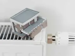Model domu na grzejniku symbolizuje wysokie koszty ogrzewania i potrzebę dopłat do prądu.
