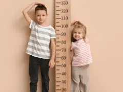 Chłopiec i dziewczynka mierzą wzrost przy drewnianej miarce. Chłopiec ma ok. 120 cm, dziewczynka ok. 80 cm.