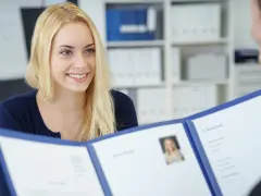 Uśmiechnięta blondynka prezentuje dokumenty, być może list motywacyjny wzór, podczas rozmowy kwalifikacyjnej.