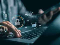 Manos sobre teclado de laptop, con iconos de seguridad digital: candado, huella, base de datos, globo terráqueo. Esto ilustra qué es la seguridad informática.