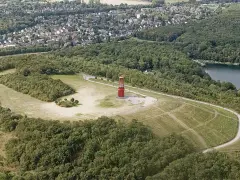 Luftaufnahme der Halde Rheinpreußen mit rotem Geleucht, umgeben von Wald und einem See.