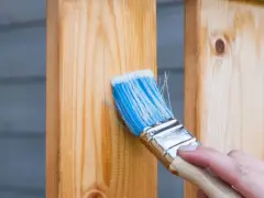 Pędzel z niebieskim włosiem nakłada na drewniany słupek ochronną warstwę, która może zawierać terpentynę balsamiczną, by zabezpieczyć drewno.