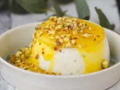 Budino fatto in casa cremoso, con salsa gialla e granella di pistacchi, servito in una ciotola bianca.