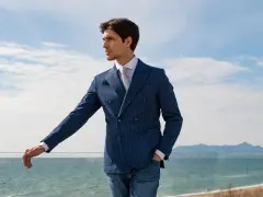 Uomo con abito doppiopetto blu a righe, camicia bianca e cravatta, jeans. Un look smart elegant dress code uomo con vista mare.
