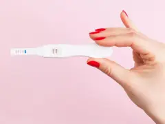 Dłoń z czerwonymi paznokciami trzyma test ciążowy z dwoma kreskami. To może być sygnał, że doszło do ciąży biochemicznej.