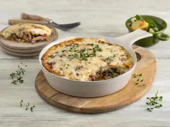 Zapiekanka makaronowa z mięsem mielonym w sosie śmietanowym, posypana serem i ziołami, podana z sałatką.