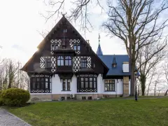 Pałac myśliwski w Promnicach, z charakterystyczną architekturą szachulcową i zdobieniami, otoczony drzewami.