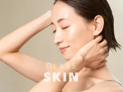 Kobieta z idealną, lśniącą cerą typu "glass skin", z dłońmi przy szyi i ramieniu.