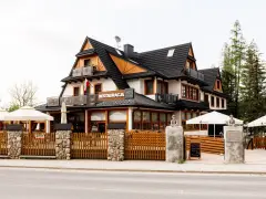 Szukasz miejsca, gdzie zjeść w Kościelisku? Ta restauracja z drewnianym ogrodzeniem i białymi parasolami zaprasza na góralskie smaki.