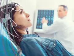 Kobieta z elektrodami na głowie podczas badania VEP. Lekarz analizuje wyniki na ekranie.