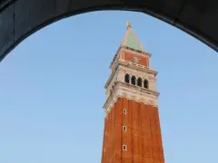 Vista dal campanile di San Marco: la torre in mattoni rossi si staglia contro il cielo azzurro, incorniciata da un arco di pietra.