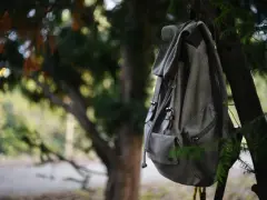 En grå ryggsäcksväska hänger från en gren i en skog. Den ser redo för ett äventyr.