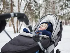 Śpiące dziecko w wózku zimą. Ciepły kombinezon, czapka i rękawiczki to podstawa, co włożyć do wózka dla noworodka zimą.