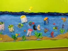 Un colorido mural de animales marinos infantiles con peces, medusas y caballitos de mar nadando en un mar azul, sobre arena.