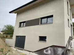 Maison moderne avec enduit neuf, une trace blanche discrète sur le crépi clair. Fenêtres noires et garage gris.