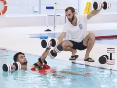 Un instructor guía a un paciente en fisioterapia acuática con pesas. Consulta el precio de fisioterapia en universidad privada para tu recuperación.