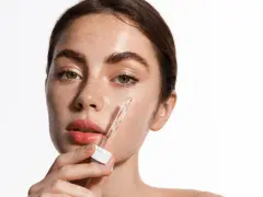 Kobieta aplikuje serum z pipetki na policzek. Skóra pełna piegów, nawilżona, z widocznym blaskiem. Kluczowe składniki: retinol i ceramidy.