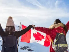 Zwei junge Frauen mit Rucksäcken und der kanadischen Flagge in den Bergen. Ein unvergesslicher Kanada Austausch!