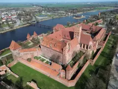 Potężny zamek z czerwonej cegły, największy zamek w Europie, otoczony murami obronnymi, nad rzeką.