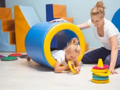 Dla kogo wczesne wspomaganie rozwoju? Dla małej dziewczynki bawiącej się w tunelu z terapeutką.