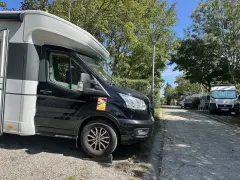 Husbil parkerad på en campingplats vid frankrike kust. Soligt väder med träd och andra husbilar i bakgrunden.