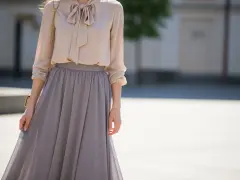Elegancka beżowa bluzka z kokardą i szara długa spódnica. Idealna stylizacja, która odpowiada na pytanie: jaka bluzka do długiej spódnicy.