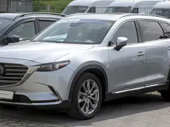 Srebrna Mazda CX-9 z napisem "PRE-OWNED" na przedniej szybie, zaparkowana na zewnątrz.