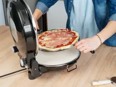 Osoba wkłada surowe ciasto na pizzę z szynką do okrągłego piekarnika.