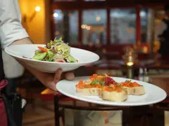 Un camarero experto demuestra cómo servir una mesa, presentando un plato de ensalada fresca y bruschettas.