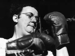 Coluche, lunettes rondes, gants de boxe, prêt à en découdre avec le racisme.