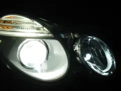 Jasny ksenon rozświetla reflektor, ukazując jego nowoczesny design i pomarańczowe kierunkowskazy.