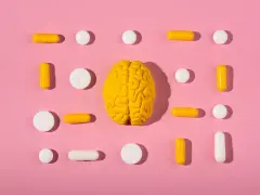 Żółty model mózgu otoczony białymi i żółtymi tabletkami i kapsułkami, symbolizującymi równowagę neuroprzekaźników, jak serotonina.