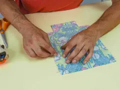 Mains assemblant deux pièces de tissu fleuri, parfait pour une idée couture débutant. Ciseaux et un chat porte-épingles à proximité.
