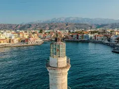 Latarnia morska wenecka w Chanii, prom na Krecie, z widokiem na port i góry w tle.