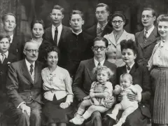 Gros plan sur une famille nombreuse posant pour une photo. On peut y voir des enfants, des adultes et des bébés. Une recherche sur Geneanet pourrait révéler leur nom de famille.