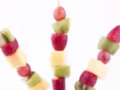 Fruktspett barnkalas med kiwi, jordgubbar, ananas och vindruvor. En färgglad och hälsosam festlig dekoration.