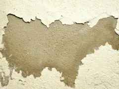 Pęknięcia na ścianie odsłaniają surowy tynk. Warstwa farby łuszczy się, tworząc nieregularne kształty.