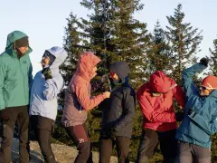 Sechs Personen in bunten Hardshelljacken stehen vor Bäumen. Eine Hardshelljacke schützt vor Wind und Wetter.