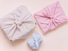 Trois paquets cadeaux joliment emballés dans des tissus de différentes couleurs (beige, rose, bleu clair). Lequel tissu pour furoshiki ? Le lin semble idéal.