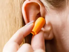 Une main insère une boule quies orange dans une oreille pour réduire les décibels.
