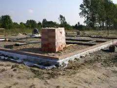 Stan zero budynku: fundamenty z cegły i betonu, piasek, folia izolacyjna, stos cegieł pod przykryciem.